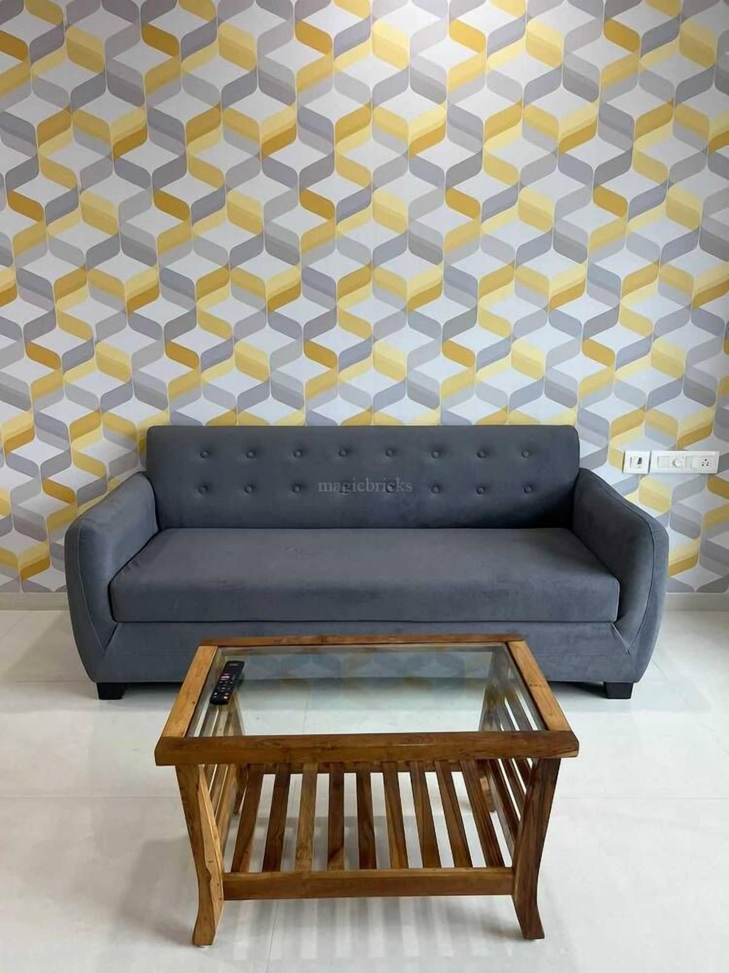 Een grijze bank tegen een behang met een geometrisch patroon, met een houten salontafel ervoor.