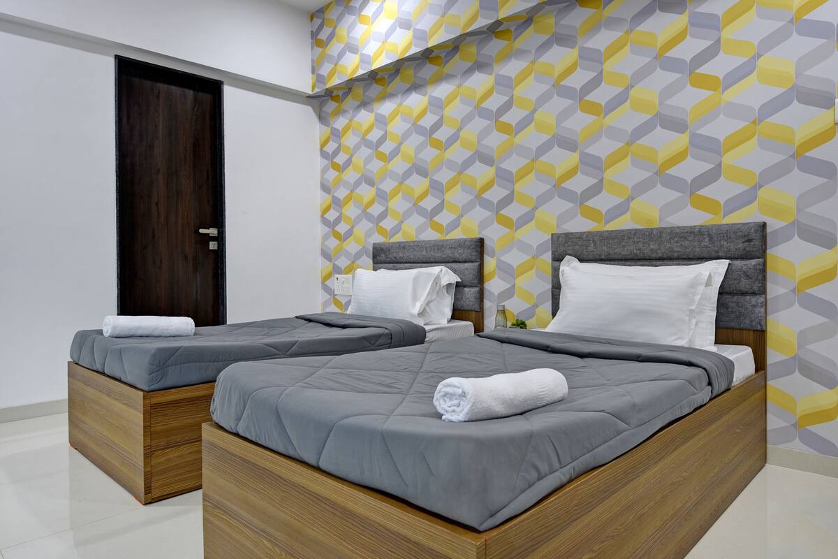 Une chambre d’hôtel moderne avec deux lits, des têtes de lit en bois et un mur orné d’un motif géométrique.