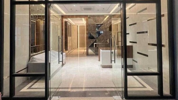 En modern hotellentrén med glasdörrar, en central trappa och en väl upplyst interiör.