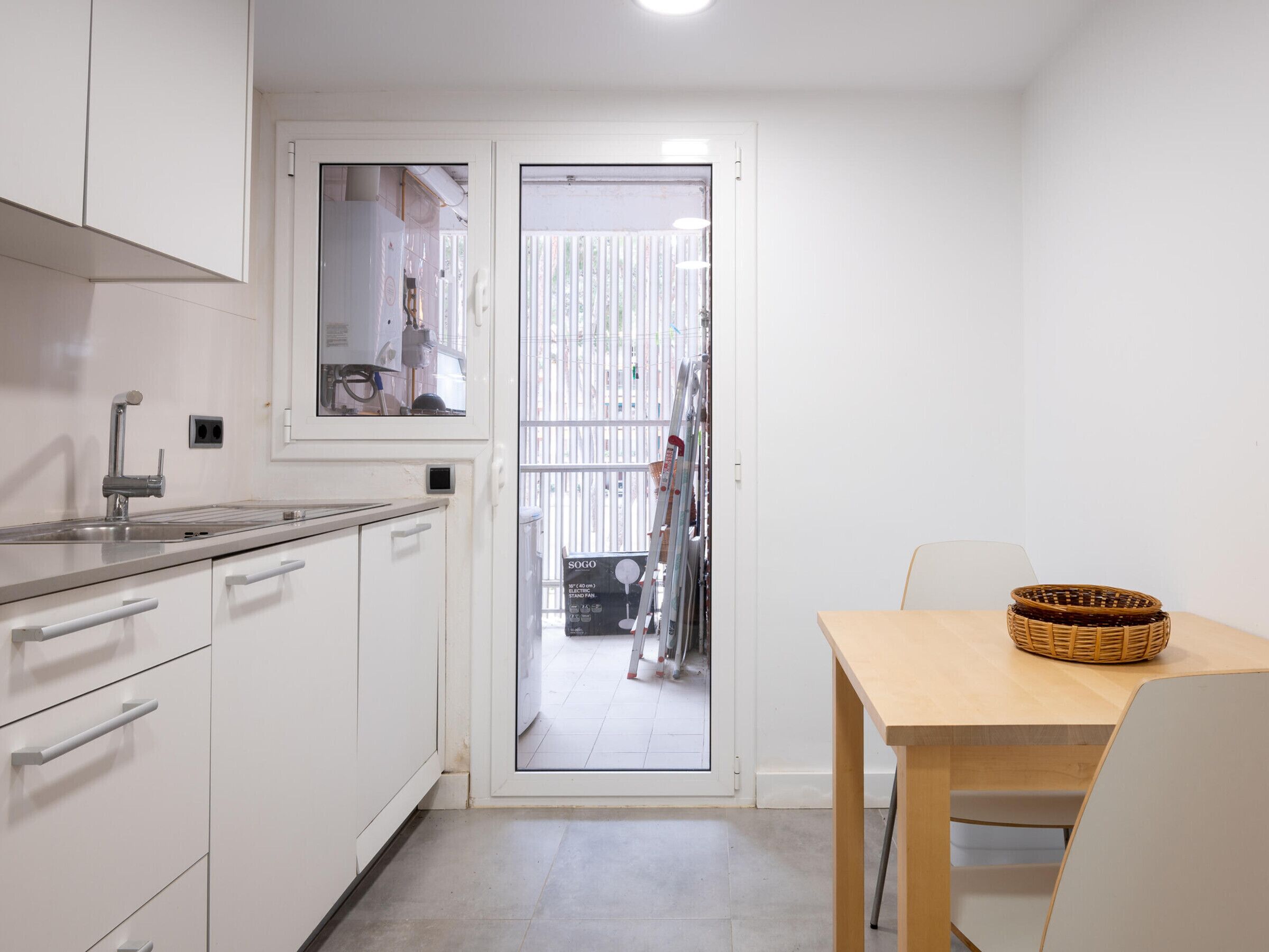 A compact kitchen with white cabinets, a stainless steel sink, and a wooden dining table with a wicker basket.