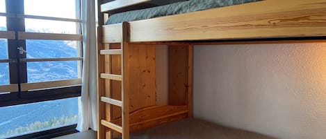 Een stapelbed met een ladder, een raam met uitzicht op een bergachtig landschap en een radiator.
