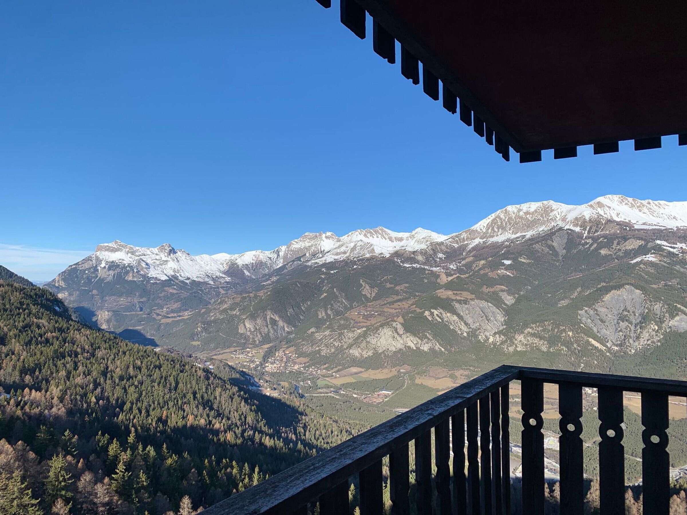 Un paysage de montagne avec des sommets enneigés et une vallée boisée.
