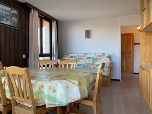 A cozy room with a wooden dining table and chairs, a sofa with a floral-patterned cover, and a wooden cabinet.