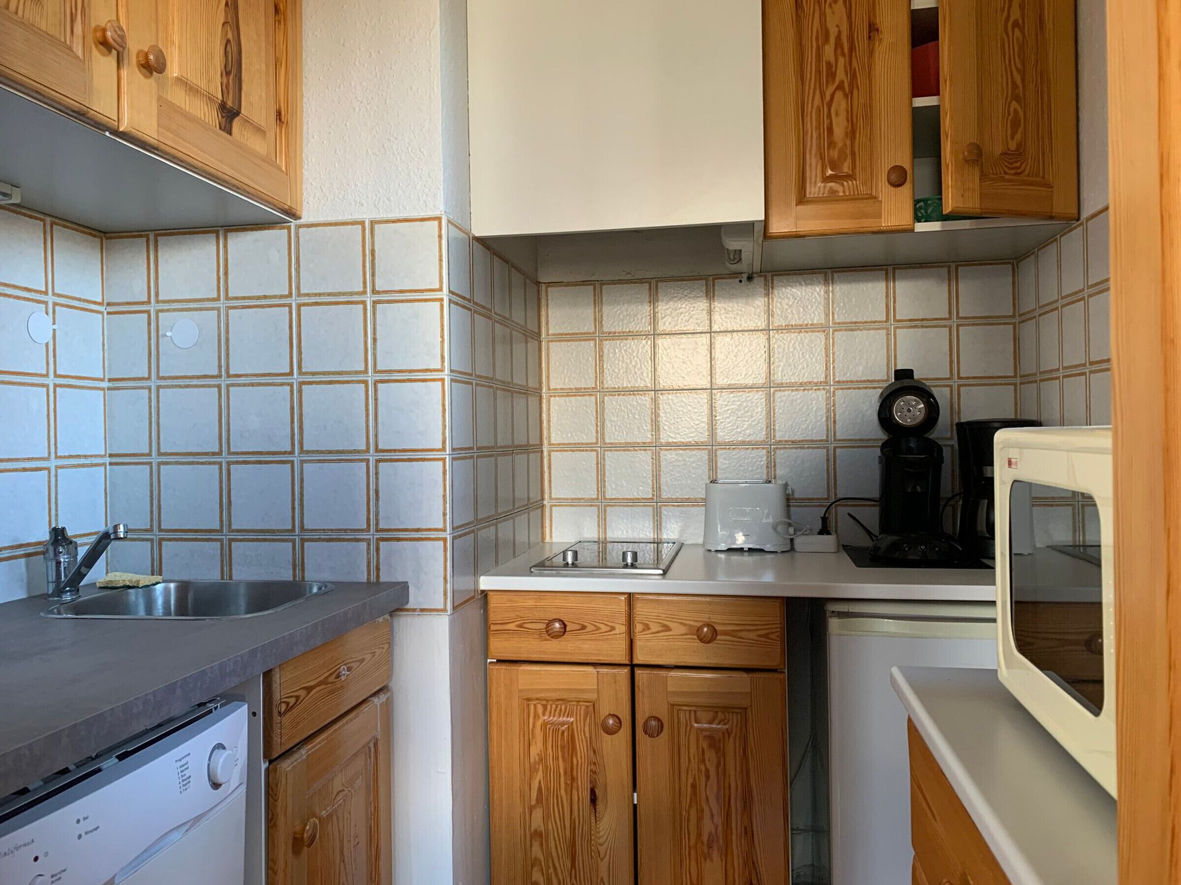 A compact kitchen with wooden cabinets, a built-in dishwasher, a toaster, and a microwave.