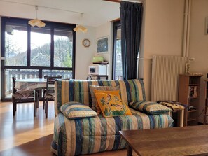 Uma sala de estar aconchegante com um sofá listrado, uma mesa de madeira e vista para o exterior através de grandes janelas.