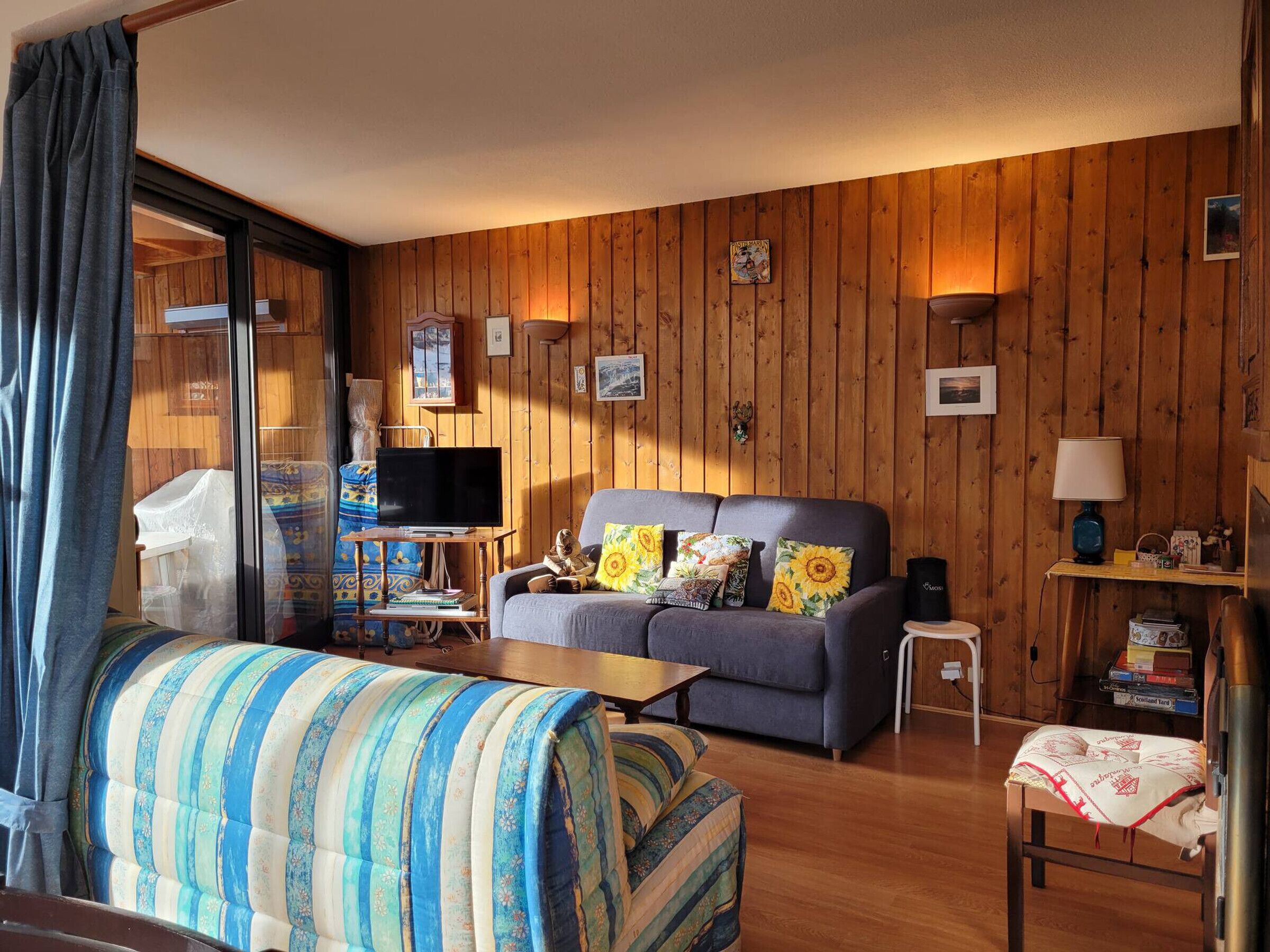 A cozy living room with a sofa, a television, and a wooden wall.