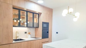 A modern kitchen with wooden cabinets, a marble countertop, a built-in microwave, and a pendant light. - Lovely Apartment at CITY QUART (Podgorica)