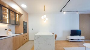 A modern kitchen with wooden cabinets, a marble island, and a built-in oven. - Lovely Apartment at CITY QUART (Podgorica)