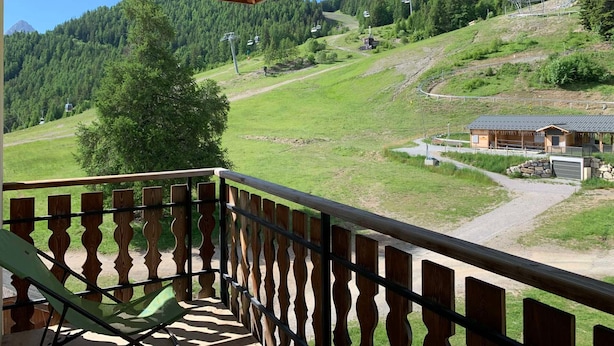 En balkon med udsigt over et bjergrigt landskab, en træbygning og en klar himmel.