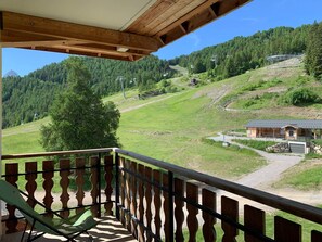 A balcony with a view of a mountainous landscape, a wooden building, and a clear sky. - Spacious, bright apartment, 3 rooms, 6 pers, slopeside (Pra-Loup)