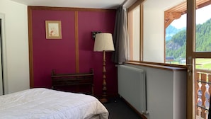 Et soveværelse med seng, radiator, lampe og et vindue med udsigt til bjerge.