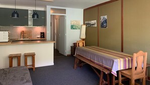 Et kompakt værelse med tekøkken, spiseplads med bænk og stole, samt seng.