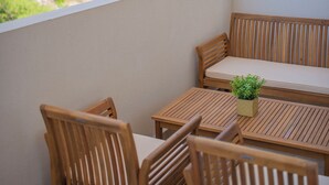 A balcony with wooden furniture, including a bench and chairs, and a small potted plant.