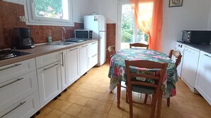 A compact kitchen with white cabinets, a microwave, a refrigerator, and a dining table with chairs. - Charming House near Beach with WIFI, Garden & Terrace - Pleumeur-Bodou (Pleumeur-Bodou)