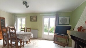 A dining area with a table and chairs, a television on a stand, and a view of greenery outside. - Charming House near Beach with WIFI, Garden & Terrace - Pleumeur-Bodou (Pleumeur-Bodou)