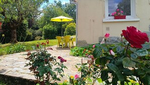 A patio area with a yellow umbrella, outdoor seating, and a window with a flower box. - Charming House near Beach with WIFI, Garden & Terrace - Pleumeur-Bodou (Pleumeur-Bodou)