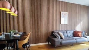 Un salon moderne avec un mur lambrissé en bois, un canapé gris agrémenté de coussins, une table à manger dressée avec des assiettes et des verres, et un luminaire suspendu.