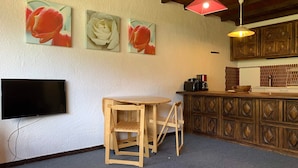 A cozy kitchen with wooden cabinets, a wooden table with two chairs, a flat-screen TV, and three wall-mounted flower paintings. - 3-room Duplex for 6 at slopes, south terrace (Pra-Loup)