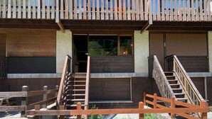 A building with a wooden staircase leading to a door, a balcony with a railing, and a view of greenery. - 3-room Duplex for 6 at slopes, south terrace (Pra-Loup)