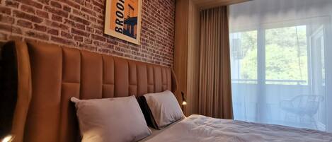 Una habitación de hotel con pared de ladrillo, una cama grande con ropa blanca y un cuadro con la imagen del Puente de Brooklyn.