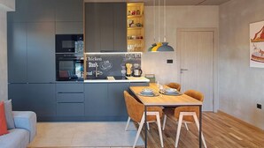 Une cuisine moderne équipée d’un four encastré, d’un four à micro-ondes et d’un tableau noir servant de menu. On y trouve une table à manger avec des chaises et un luminaire suspendu.