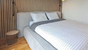 Une chambre à coucher moderne avec un lit, deux lampes fixées au mur et un mur décoré de lattes en bois.