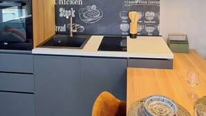 Une cuisine moderne dotée d’un four encastré, d’un tableau affichant la carte des cafés et d’une étagère en bois où sont rangés les ustensiles de cuisine.