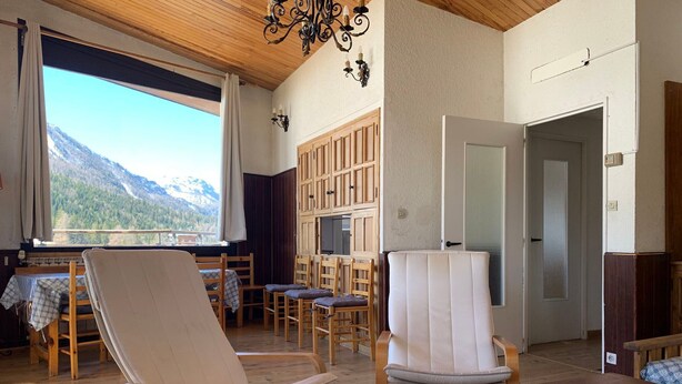 Ein Zimmer mit Holzboden, einem großen Fenster mit Bergblick, einem Holzesstisch und mehreren Stühlen.