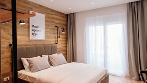 A modern bedroom with a wooden accent wall, a large bed with white linens, a headboard, and a window with sheer curtains. - Comfortable Apartment at CITY QUART (Podgorica)