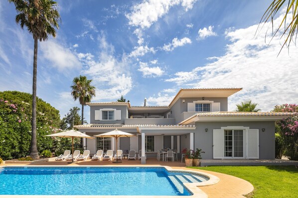 A two-story house with a swimming pool, outdoor seating, and a garden.
