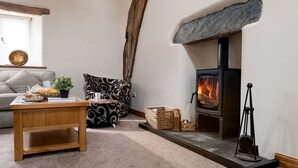 A cozy living room with a stone fireplace, a sofa, a coffee table, and a rustic wooden beam.