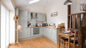 A modern kitchen with light grey cabinets, a wooden dining table, and a rustic wooden staircase. - Gorse Barn Summary:<br>E (Conwy Principal Area)
