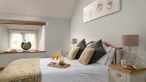 A bedroom with a bed, bedside table, lamp, and a window with a decorative item. - Gorse Barn Summary:<br>E (Conwy Principal Area)