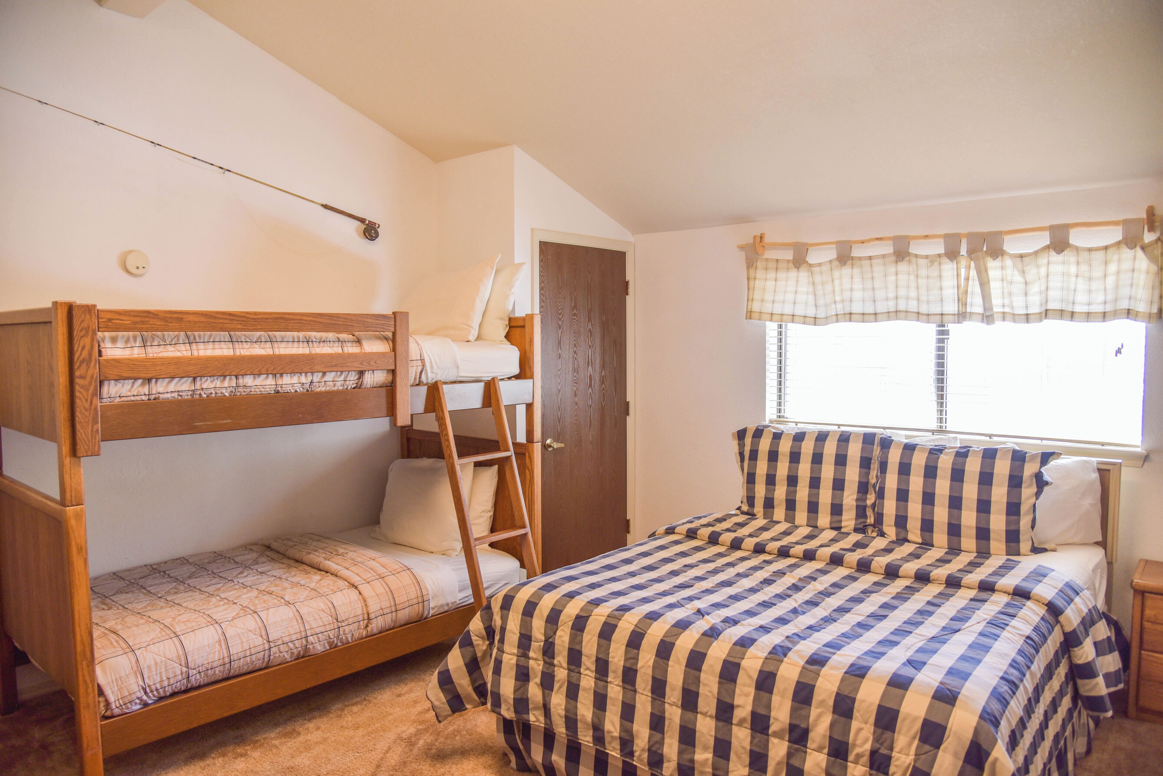 A bedroom with a bunk bed, a single bed, a window with curtains, and a wooden ladder.