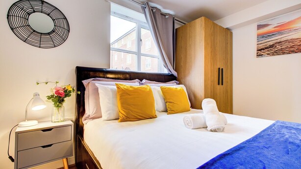 A neatly made bed with white and yellow pillows, a blue blanket, and rolled towels on a wooden headboard. - Spacious 2-bed Apartment, Family With Pets Welcome (London)