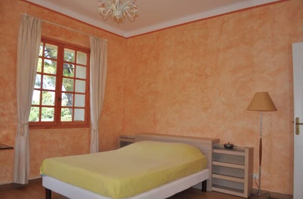 Een slaapkamer met een bed, nachtkastje, lamp en raam met gordijnen.