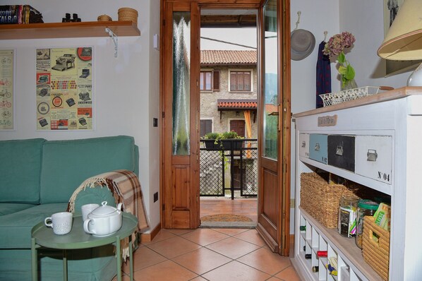 A cozy living room with a green sofa, a small table with two white mugs, and a wooden door leading to a balcony with plants. - Casa Anna by Wonderful Italy (Bellagio)