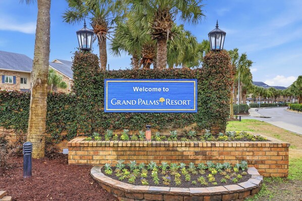 Een bord dat bezoekers verwelkomt bij Grand Palms Resort, omgeven door weelderige begroeiing en palmbomen.