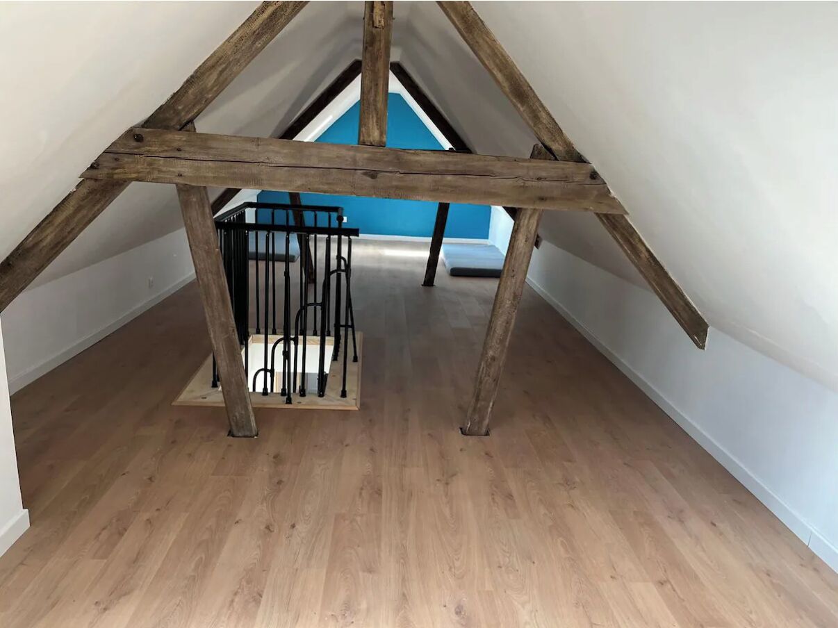 An attic room with exposed wooden beams, a black metal railing, and a blue wall in the background.
