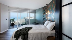 A modern bedroom with a large bed, a view of the sea through a sliding glass door, and a decorative wall panel. - Amazing Sea View Stylish 1BR | Safe Room on Floor (Herzliya)