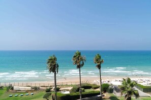 A beachfront hotel with a view of the ocean, palm trees, and a sandy beach.