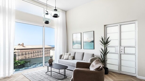 A modern living room with a sofa, armchair, and coffee table, large windows with a view, and a potted plant.