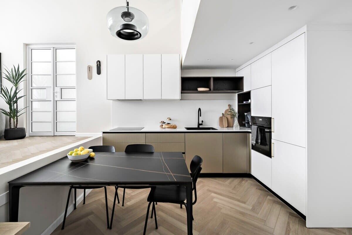 A modern kitchen with white cabinets, a black dining table, and a potted plant.