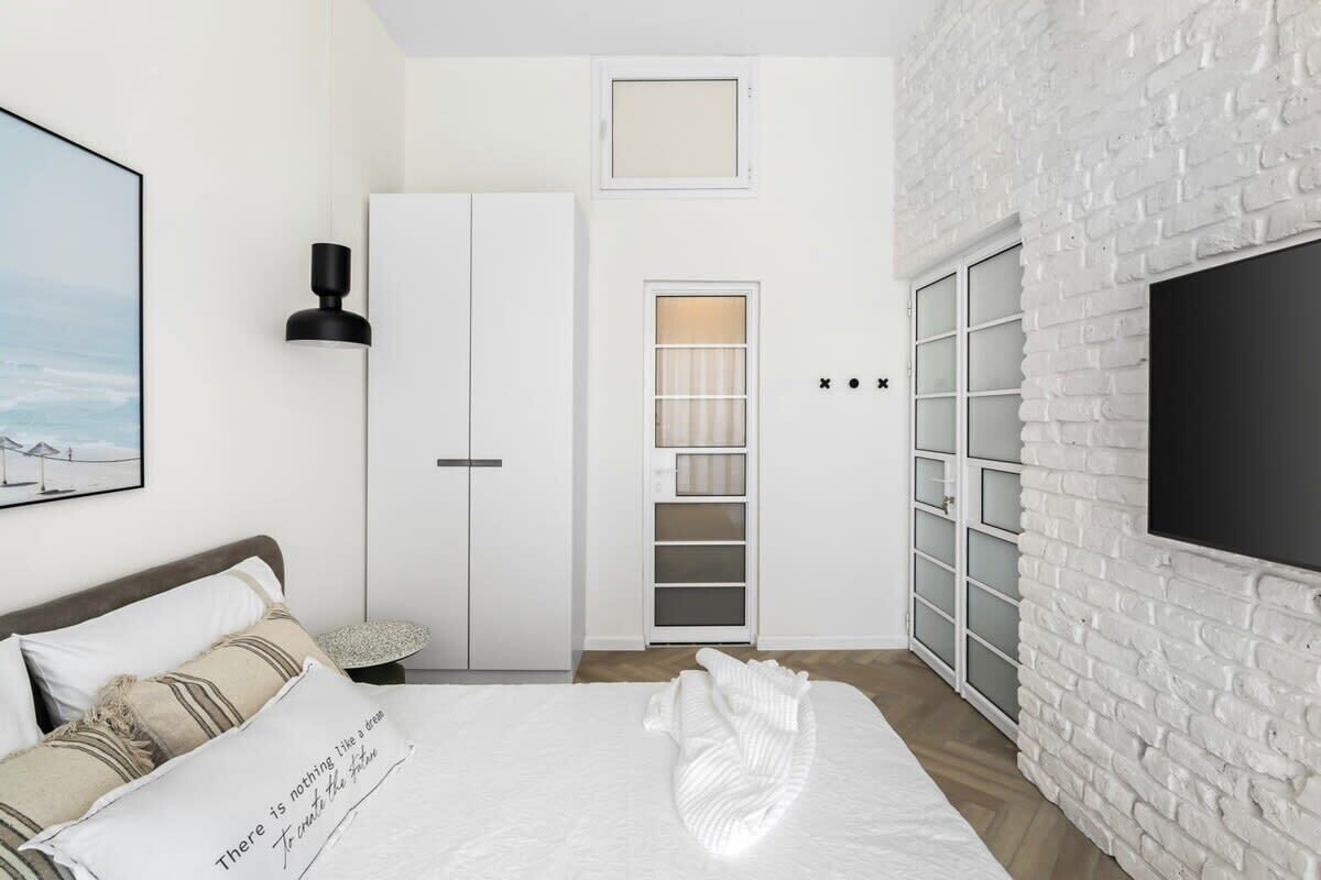 Une chambre à coucher avec un lit, une armoire, une télévision et un mur en briques blanches.