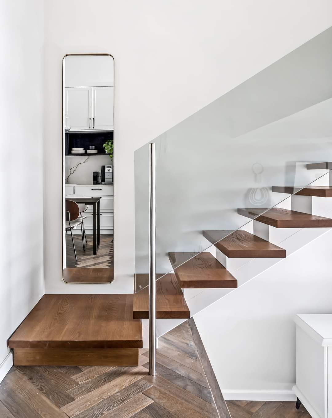 A modern staircase with wooden steps and glass railings, leading to a white interior space.