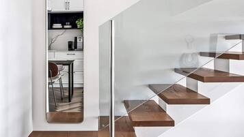 A modern staircase with wooden steps and glass railings, leading to a white interior space.