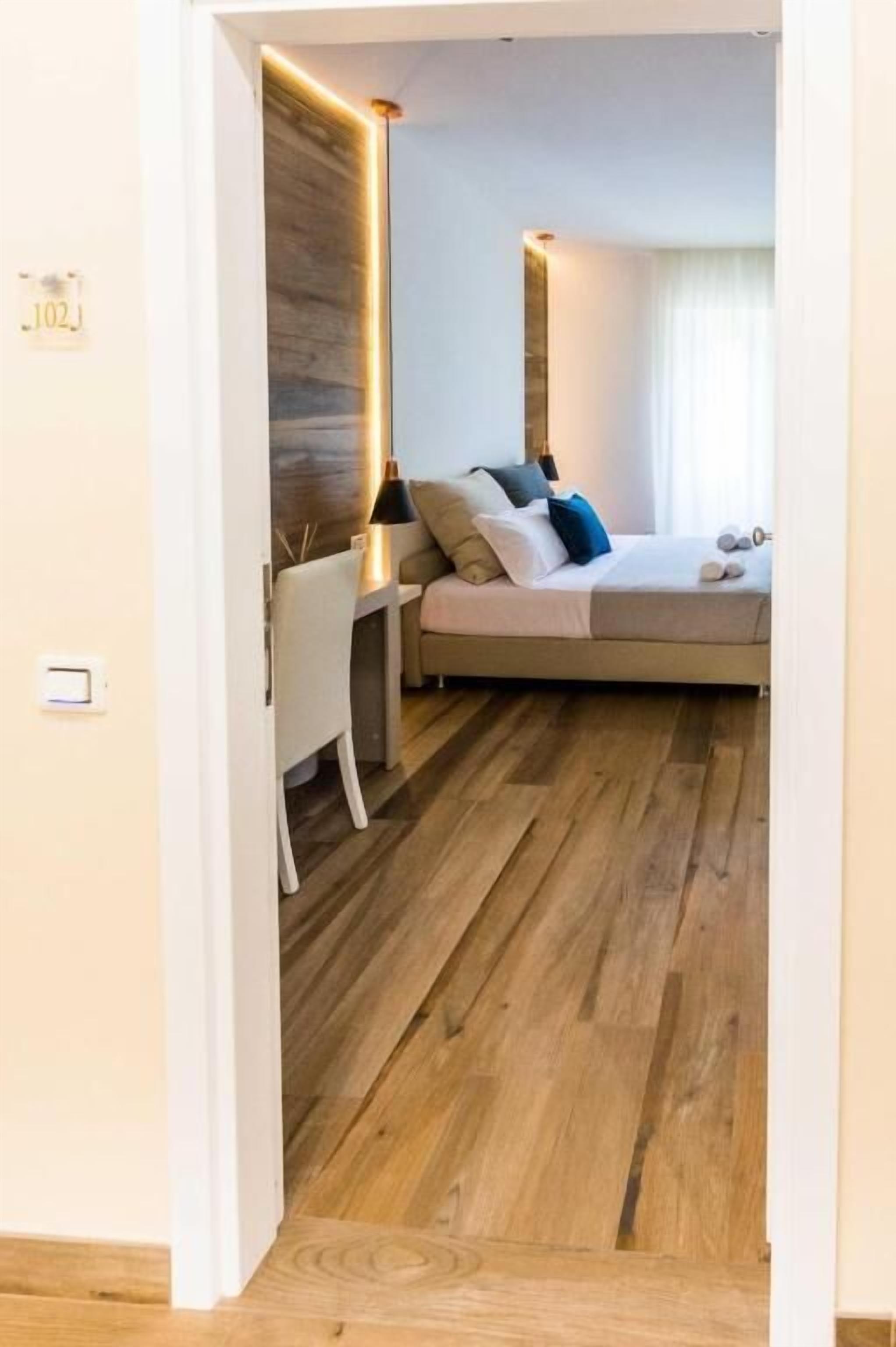 Un dormitorio moderno con piso de madera, una cama con almohadas, una mesita de noche y una lámpara.