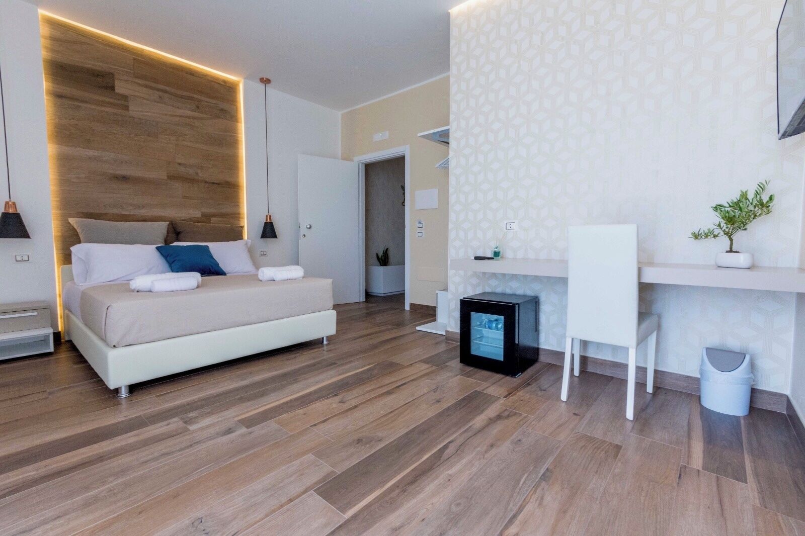 A modern bedroom with a bed, bedside table, and a small black refrigerator.