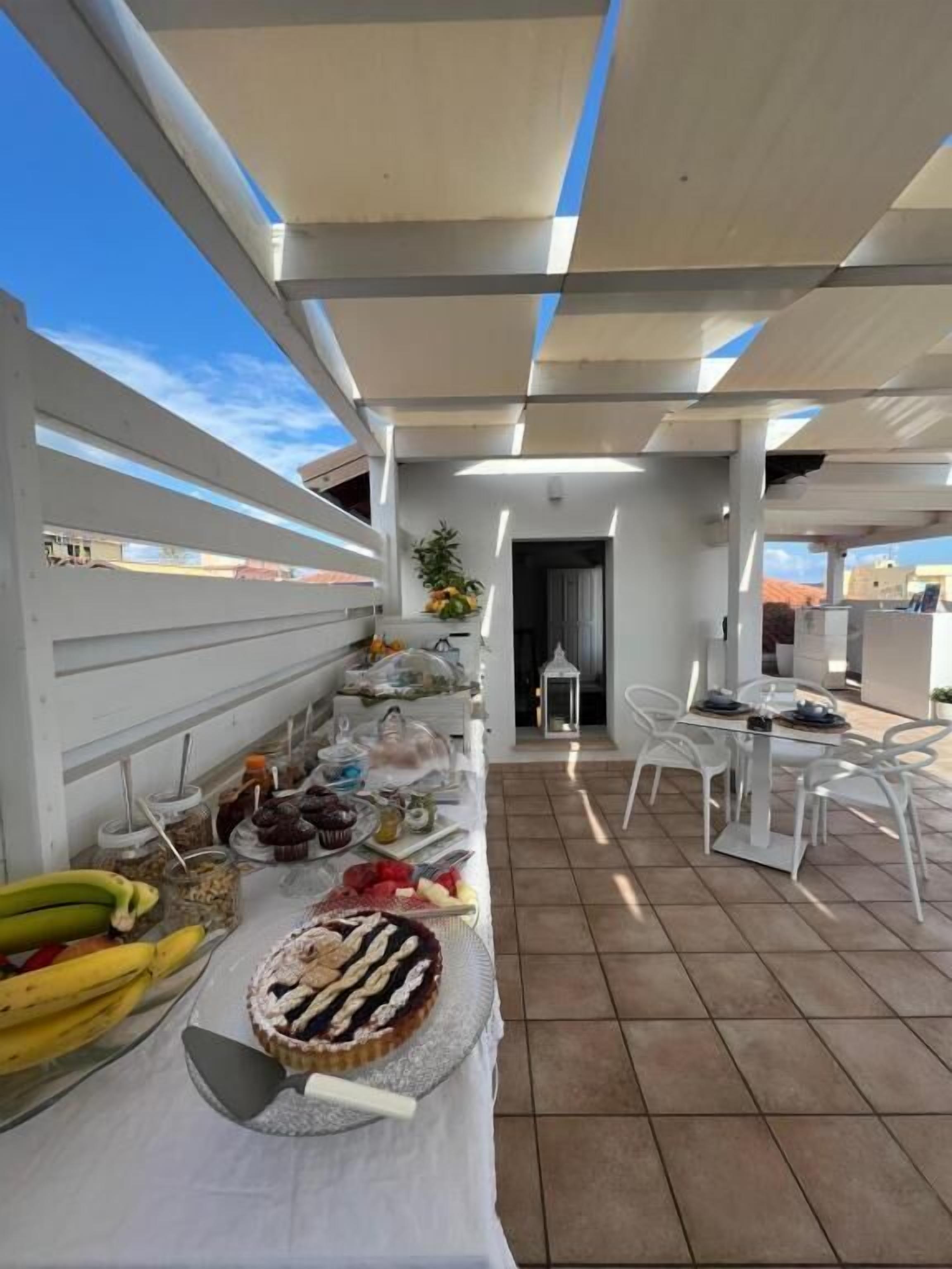 An outdoor dining area with a table set for a meal, including fruits, pastries, and a pie.