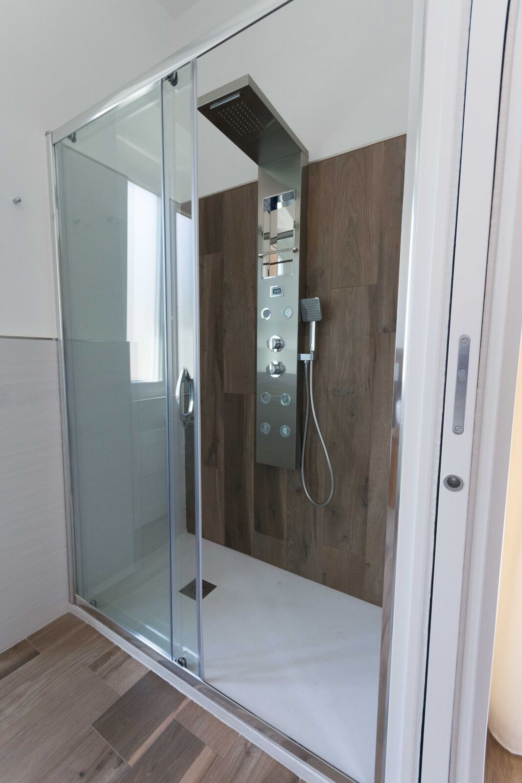 A modern shower enclosure with a glass door, a control panel with multiple settings, and a showerhead.